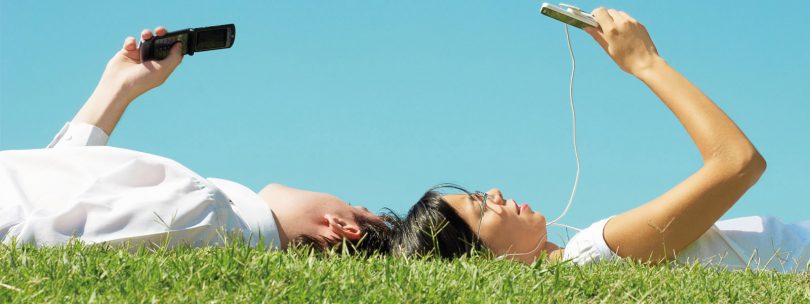два человека лежат на траве с телефонами