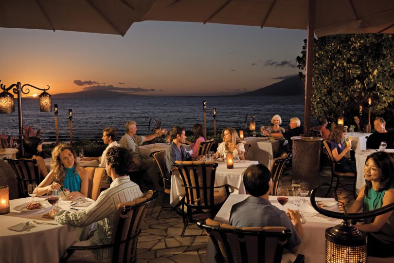 люди сидят за столиками в ресторане у моря
